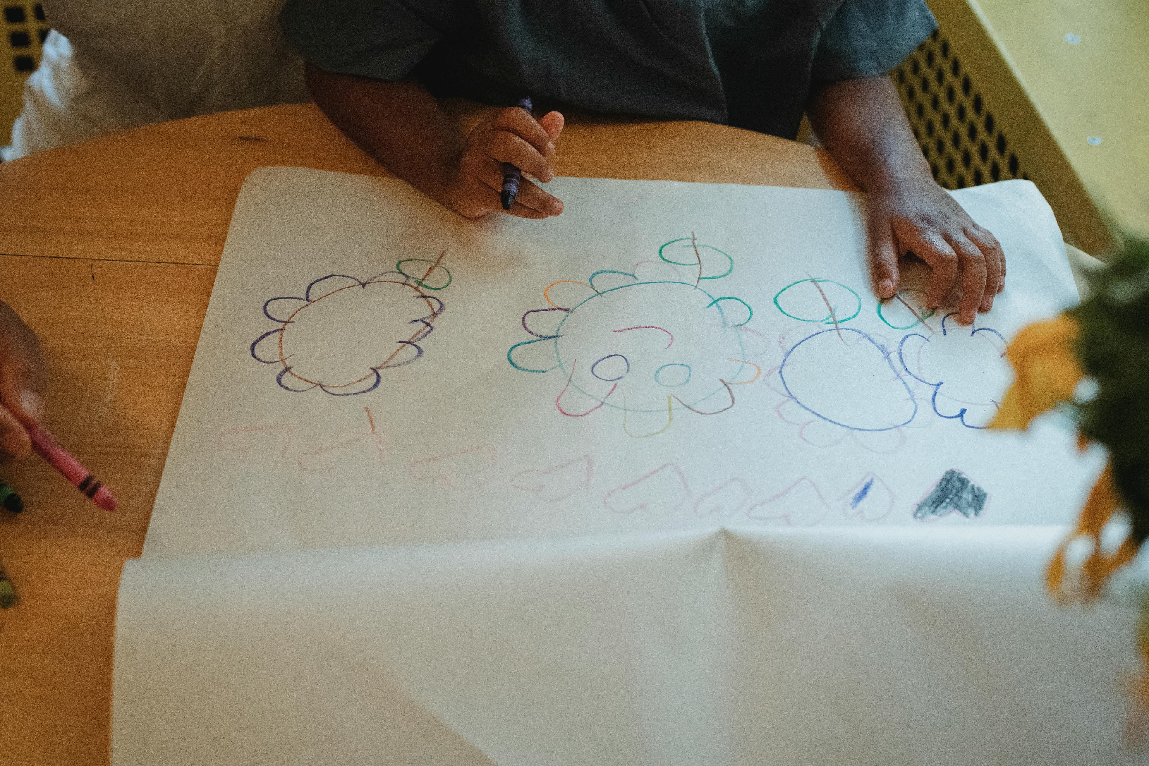 Bambino disegna fiori e soli con i pastelli su un foglio